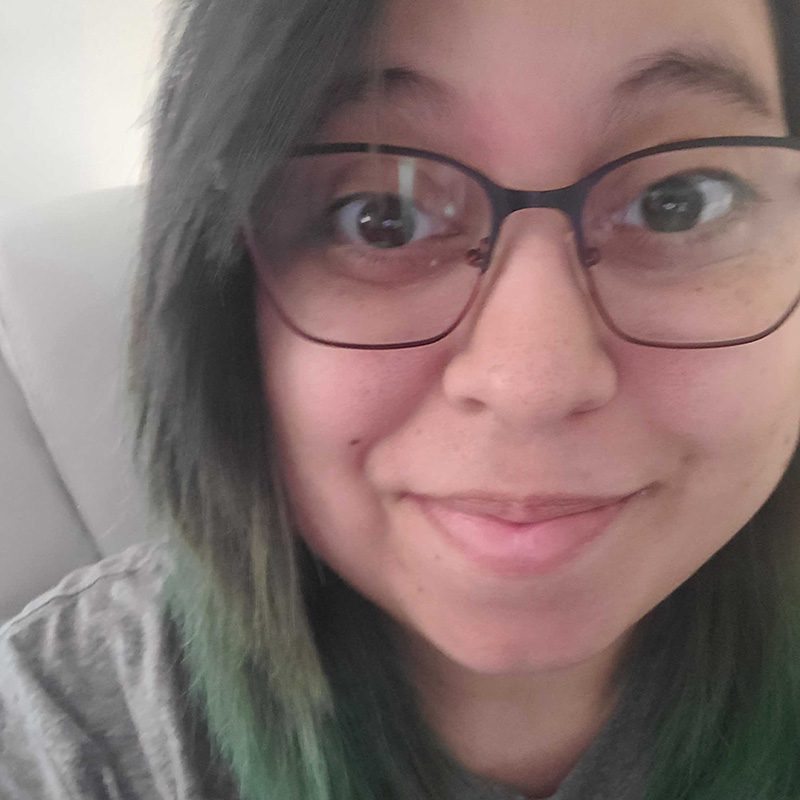 Mia Delgado smiling with glasses and a green streak in her hair